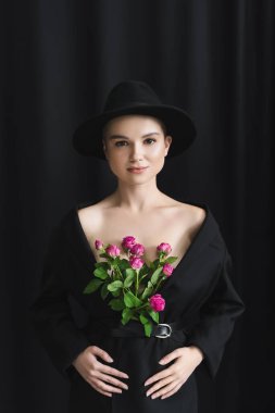 Siyah ceketli, pembe güllü, siyah arka planda genç bir kadının ön görüntüsü.