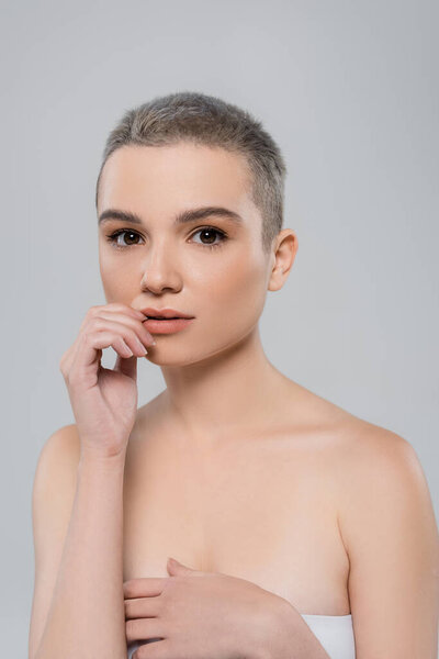 pretty woman with short hair touching lips and looking at camera isolated on grey