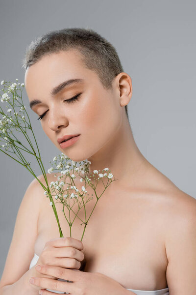 sensual woman with closed eyes near branches of white gypsophila isolated on grey