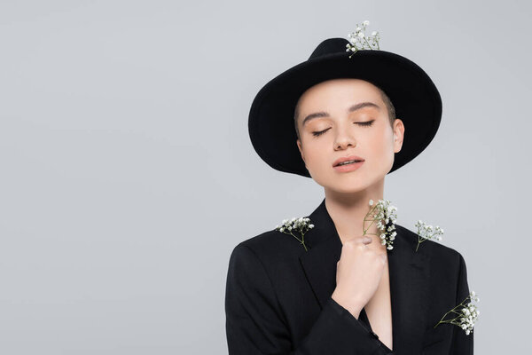 sensual woman with closed eyes and white tiny flowers on black blazer posing isolated on grey