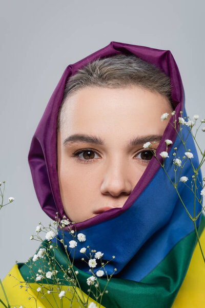 портрет молодой женщины с флагом lgbt на голове рядом с цветами гипсофилы изолированы на сером