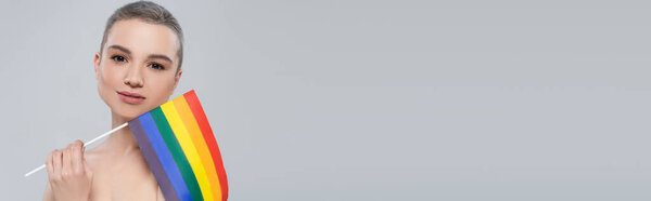 женщина с короткими волосами, держа небольшой флаг lgbt изолированы на сером, баннер