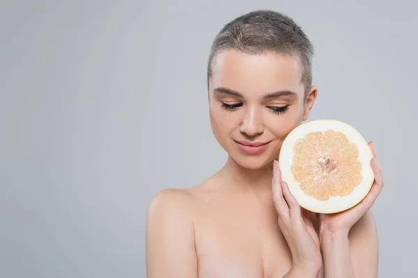 smiling woman with naked shoulders holding half of ripe grapefruit isolated on grey
