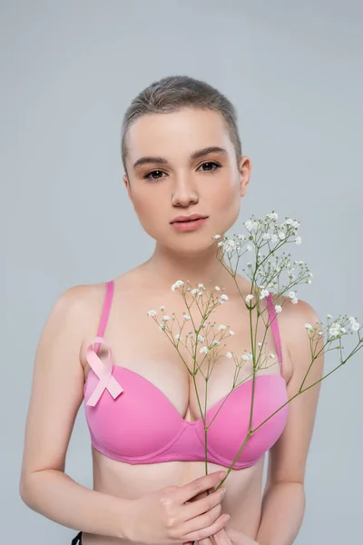ピンク色の意識リボンを持つ若い女性は グレーに孤立した小さなジプシーの花を持っています — ストック写真