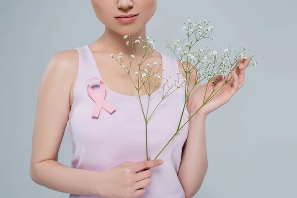 cropped view of woman in tank top posing with pink awareness ribbon and gypsophila flowers isolated on grey