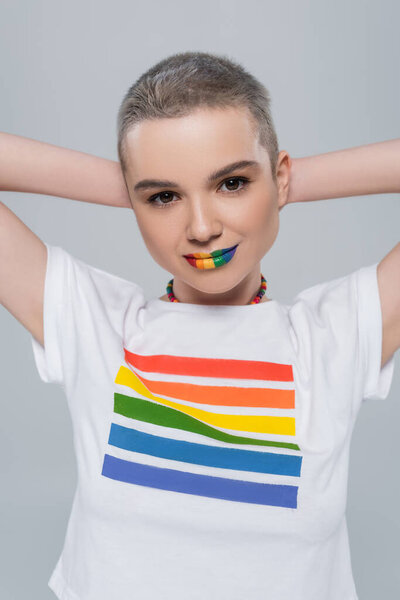 красивая женщина с радужными цветами губы стоят с руками за головой изолированы на сером