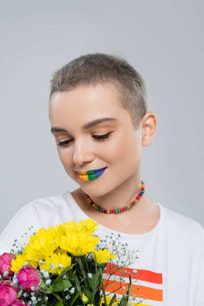 очаровательная женщина с радужными цветами губы держа цветы изолированы на серый