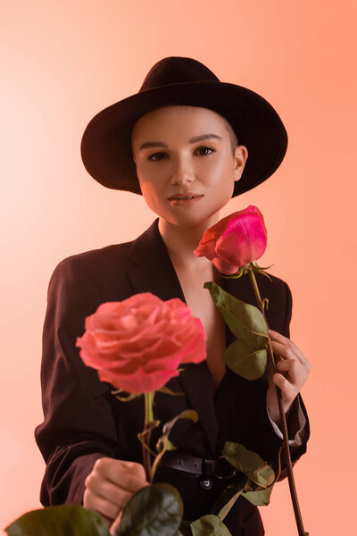 elegant woman with pink roses looking at camera on coral background
