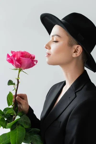 side view of trendy woman with natural makeup holing pink rose isolated on grey