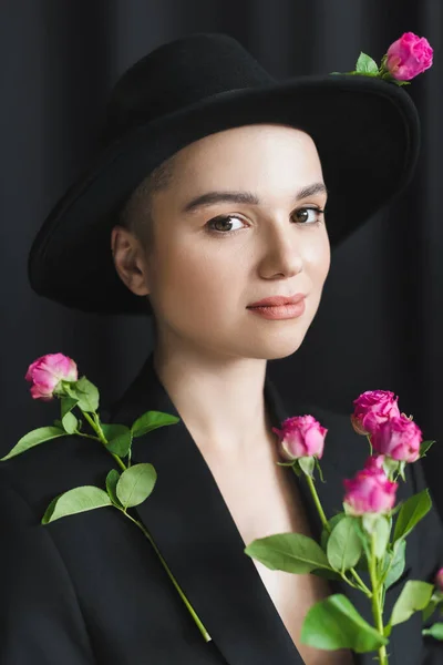 pretty woman with natural makeup looking at camera near small pink roses on black