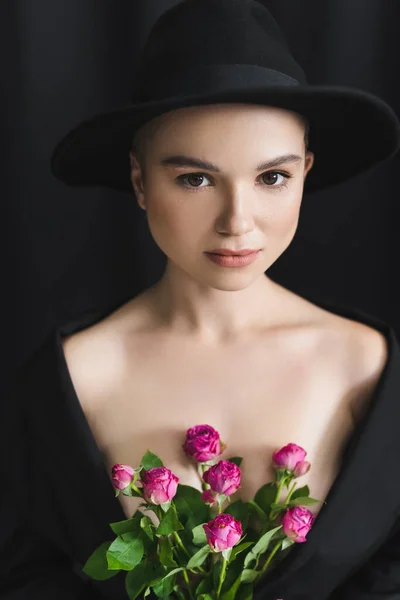 戴着帽檐的年轻女子 戴着粉红色的小玫瑰 望着黑色的相机 — 图库照片