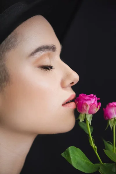 profile of young woman near pink tiny roses isolated on black