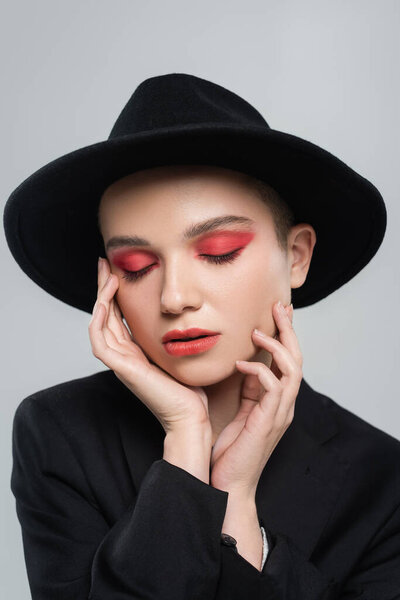 woman with closed eyes and carmine red makeup touching face isolated on grey