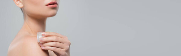 обрезанный вид женщины, держащей кубик льда рядом с голым плечом изолирован на сером, баннер