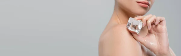 灰色のバナーに隔離された裸の肩に氷のキューブを適用する女性の部分的なビュー — ストック写真