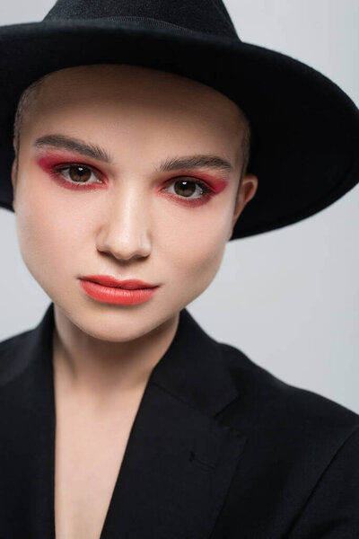 portrait of young woman with carmine red makeup, wearing black fedora hat isolated on grey
