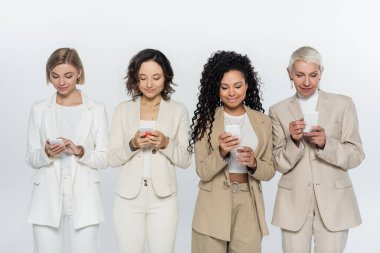 Gri, feminizm kavramına izole edilmiş cep telefonları kullanan gülümseyen ırklar arası iş kadınları