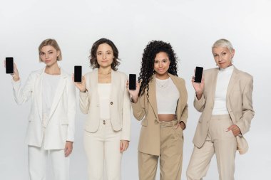 Gri ekranda boş ekranlı akıllı telefonları tutan çok ırklı iş kadınları 