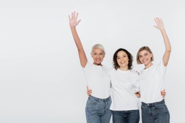 Beyaz tişörtlü gülümseyen kadınlar gri feminizm kavramına izole edilmiş el sallıyorlar.