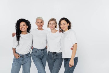 Happy multiethnic women in white t-shirts hugging isolated on grey  clipart