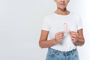 Göğüs kanserinin pembe kurdelesini tutan yaşlı bir kadının gri renkte izole edilmiş görüntüsü. 