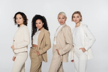 Multiethnic businesswomen in formal wear posing isolated on grey, feminism concept clipart