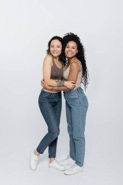 Gülümseyen Afrikalı Amerikalı kadın. Gri arka planda dövmeli arkadaşına sarılıyor. 