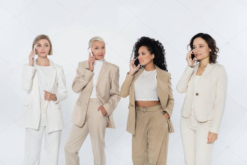 Multiethnic businesswomen talking on mobile phones isolated on grey 