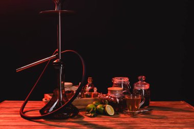 Çay, taze limon ve nargile. Ahşap masada, siyah ışıkta izole edilmiş.