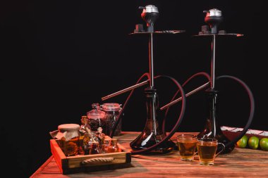 Nargilelerin yanında çay fincanları ve siyah üzerine izole edilmiş ahşap yüzey limonları. 
