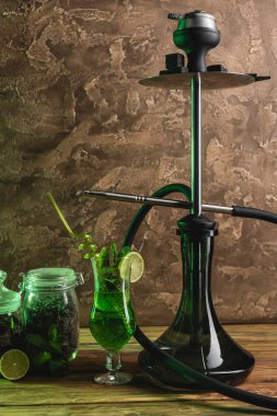 Kokteyl yanında nargile ve kavanozlarda çay ahşap yüzeyde dokulu taş arka planda. 