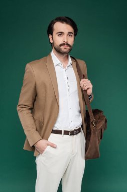 Bıyıklı adam cebinde ve koyu yeşil üzerinde deri çanta tutuyor. 