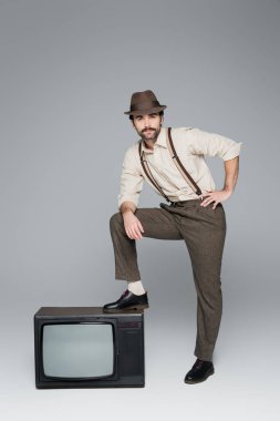 full length of man vintage style clothing posing with hand on hip near antique tv on grey clipart