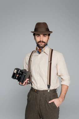 Eski moda giysiler ve eski model kameralar taşıyan şapkalar ve gri renkte el ele duran bir adam. 