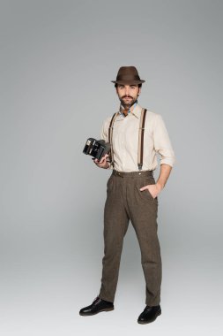 Tam boy erkek retro tarzı kıyafetler ve eski model kamera taşıyan şapka ve gri cepte duran. 