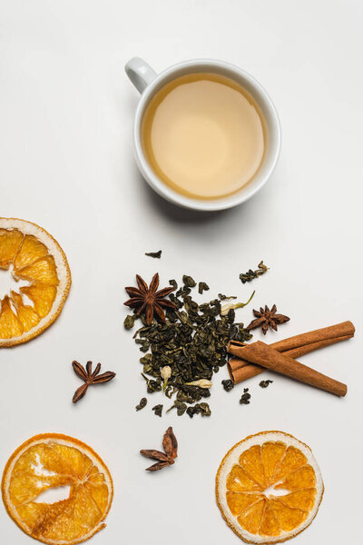 Top view of cup of tea near dry spices and orange slices on white background 