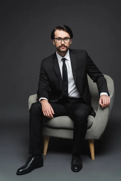 Hombre Negocios Con Traje Gafas Sentado Sillón Gris Oscuro —  Fotos de Stock