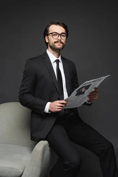 Businessman Suit Glasses Leaning Armchair Holding Business Newspaper Dark Grey — Stock Photo, Image