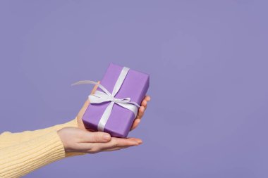 Kırpılmış genç kadın elinde paketlenmiş bir hediye kutusuyla mor renkte izole edilmiş.