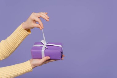 Mor üzerine izole edilmiş paketlenmiş hediye kutusunda kurdele çeken genç bir kadın görüntüsü.