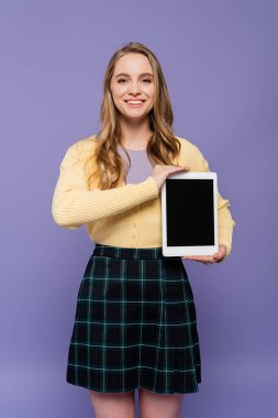 Mor üzerine izole edilmiş boş ekranlı dijital tablet tutan mutlu genç kadın.