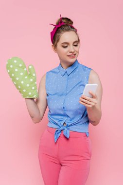 Pembe üzerine izole edilmiş akıllı telefon kullanan yeşil fırın eldivenli mutlu genç bir kadın.