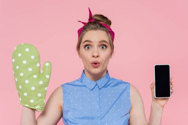Yeşil fırın eldivenli genç bir kadın elinde pembe ekranda boş ekranlı akıllı bir telefon tutuyor.