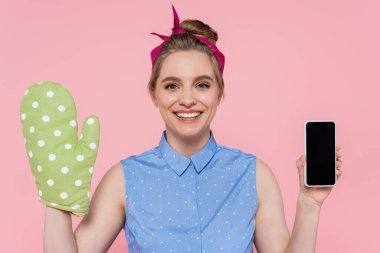 Yeşil fırın eldivenli mutlu genç kadın pembe ekranda izole edilmiş akıllı telefon tutuyor.