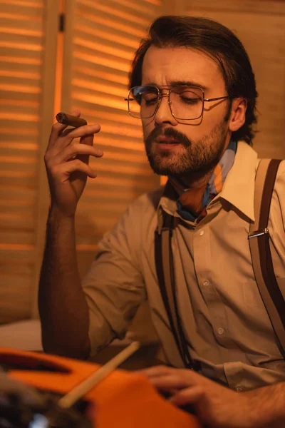 带着胡子和眼镜的记者在模糊的复古打字机旁抽雪茄 — 图库照片
