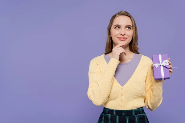 Wanita Muda Pensif Memegang Kotak Hadiah Dibungkus Terisolasi Pada Ungu — Stok Foto