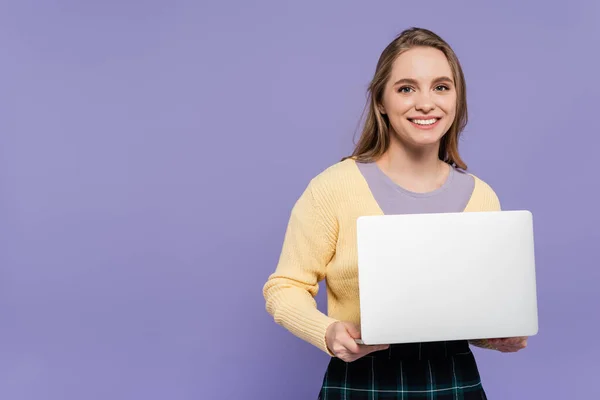 一个快乐的年轻女人拿着用紫色隔离的笔记本电脑 — 图库照片