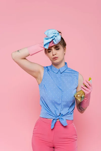身穿橡胶手套 手持蓝色破布 用粉色隔离的喷雾器的疲惫的年轻女子 — 图库照片