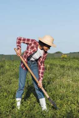 full length view of african american woman in straw hat digging in field clipart