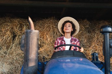 african american woman looking away while driving tractor on farm clipart